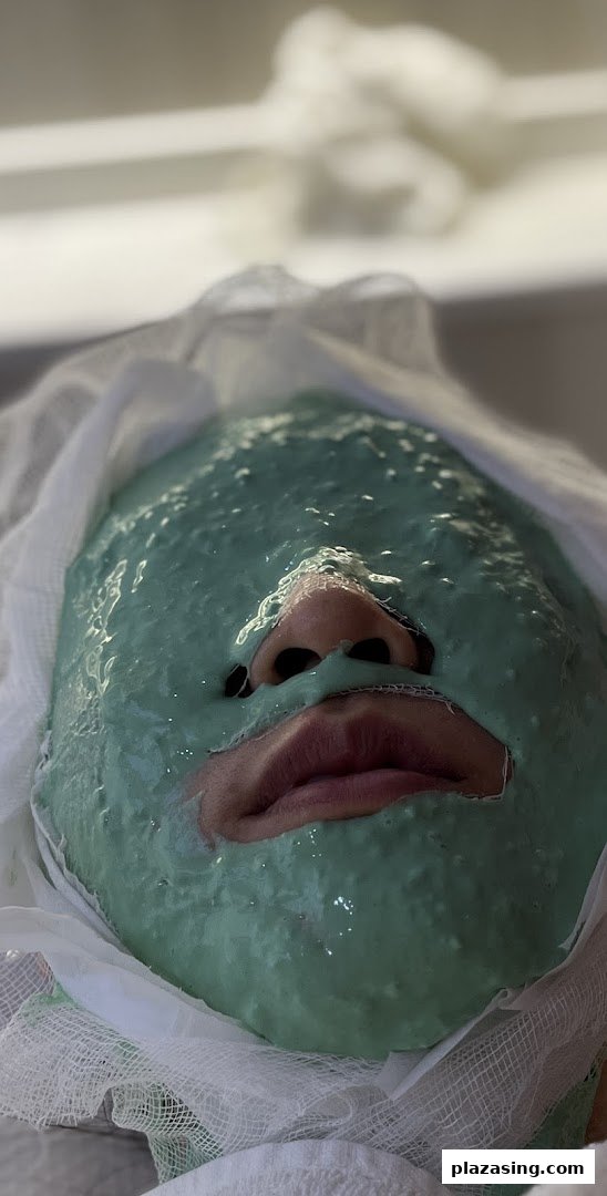 A person receiving a green facial mask treatment at Shakura Pigmentation Beauty.