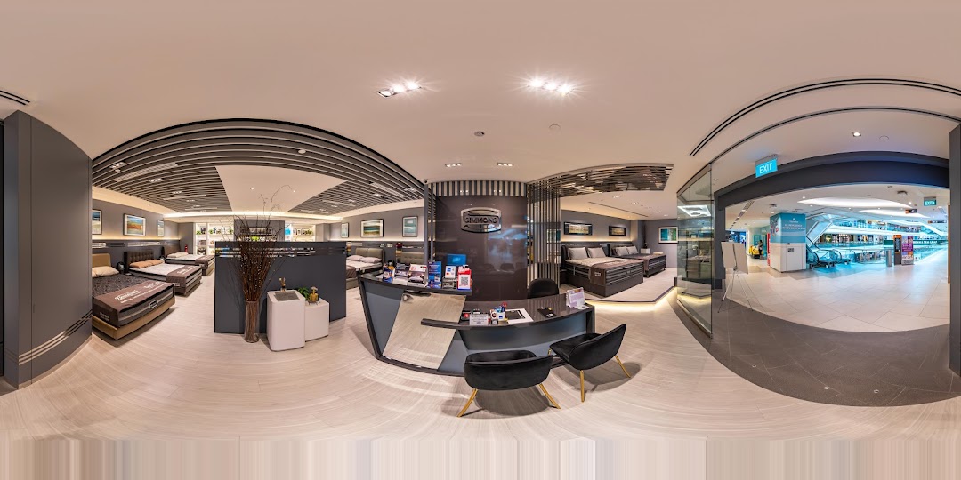 An interior panoramic view of Simmons Studio, showcasing various mattresses, beds, and a reception desk.