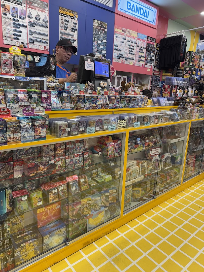 Interior view of Simply Toys, showcasing display cases filled with trading cards and collectibles, with a staff member at the counter.