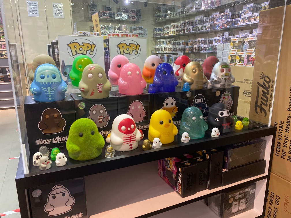 A vibrant display of collectible figures, including 'Tiny Ghost' and Funko Pop! boxes, inside a toy shop.