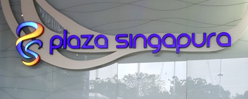 Close-up of the illuminated 'Plaza Singapura' mall logo and name.
