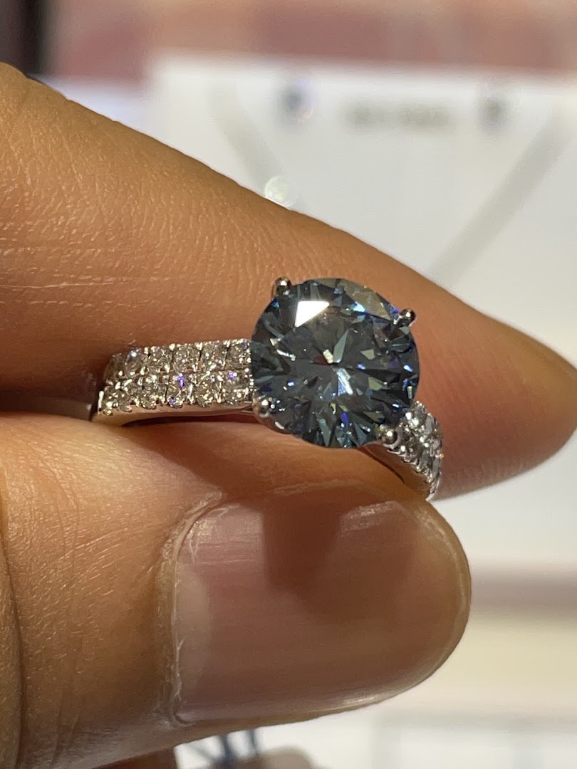 A hand holds a stunning ring featuring a large blue gemstone and a diamond-encrusted band.