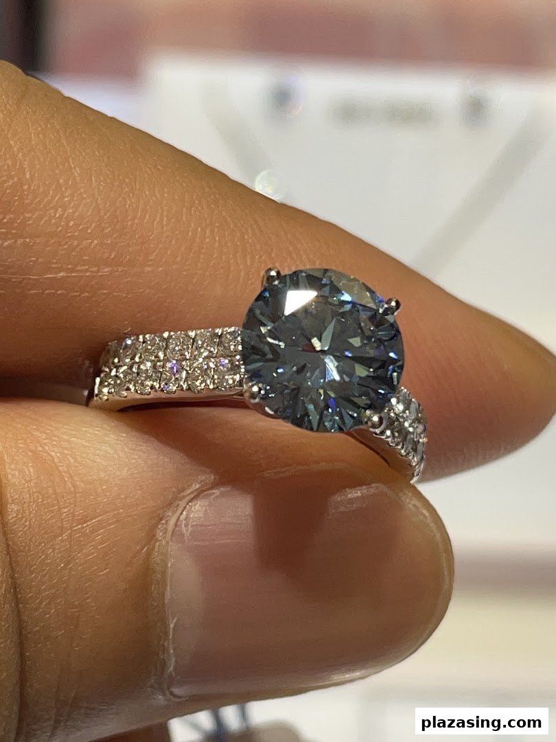 A hand holds a stunning ring featuring a large blue gemstone and a diamond-encrusted band.
