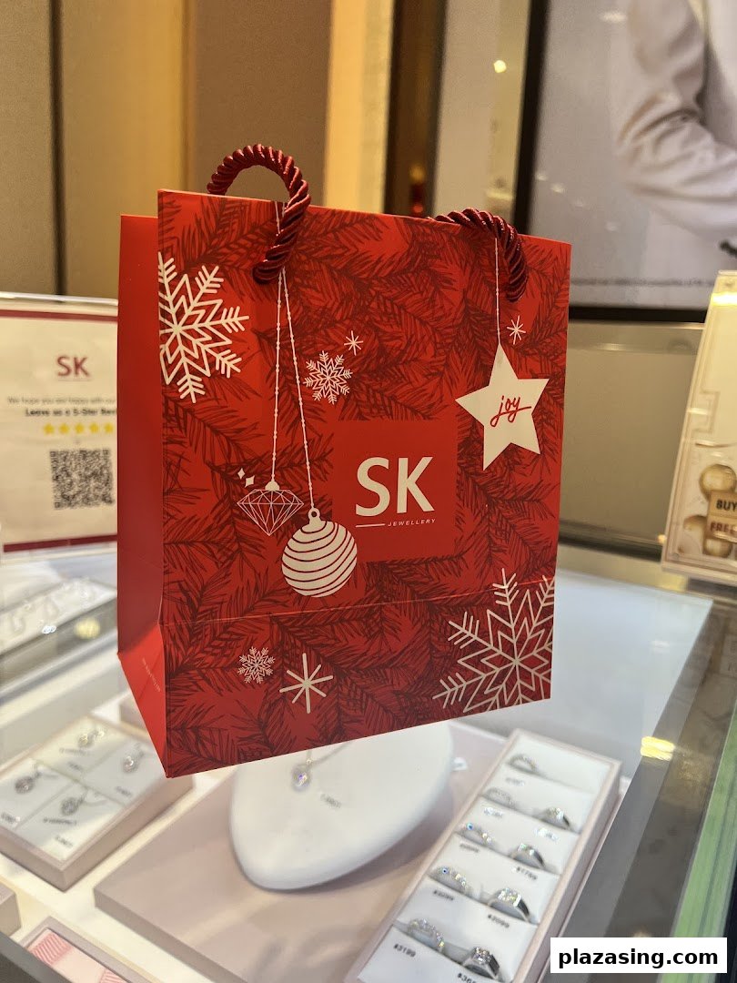 A festive red SK Jewellery shopping bag displayed amidst sparkling jewellery in a retail setting.