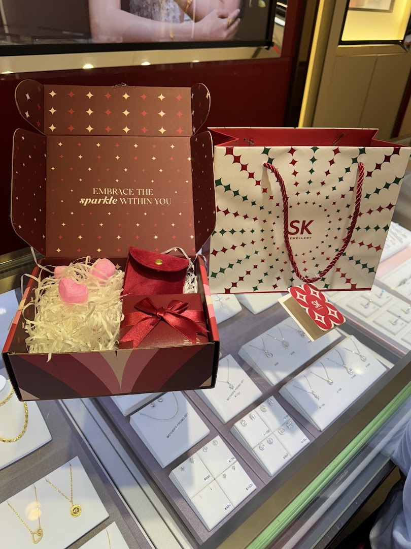 An open gift box, SK Jewellery shopping bag, and sparkling jewellery displays inside the store.