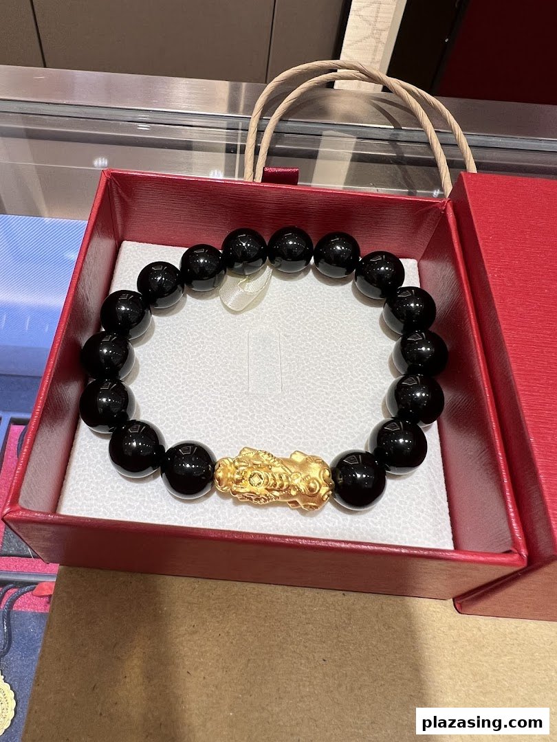 A black beaded bracelet featuring a prominent gold Pixiu charm, presented in a red gift box.