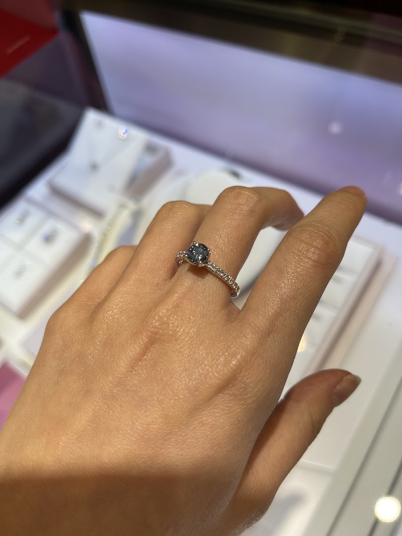 A hand models a beautiful ring with a dark gemstone and diamond-studded band.