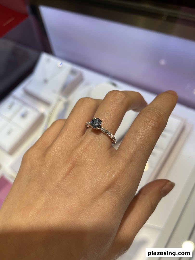 A hand models a beautiful ring with a dark gemstone and diamond-studded band.