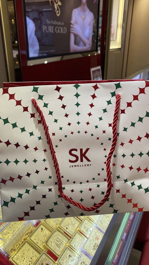 An SK Jewellery shopping bag with gold items and a promotional display in the background.