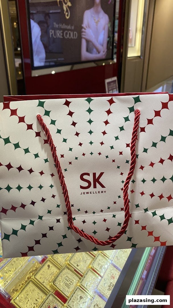 An SK Jewellery shopping bag with gold items and a promotional display in the background.