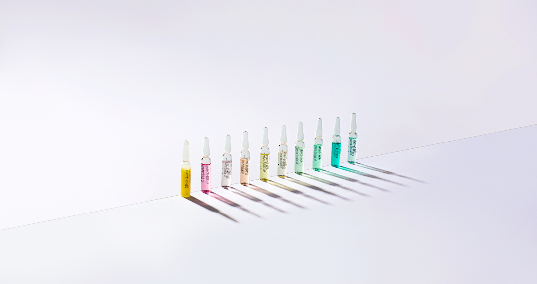 A row of colorful SkinLab ampoules casting shadows on a white surface.