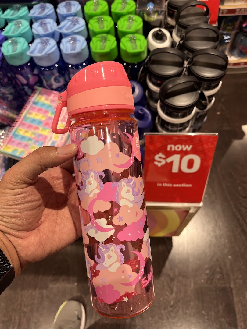 A hand holds a pink unicorn-themed Smiggle water bottle, with other colorful bottles and a '$10' sale sign.
