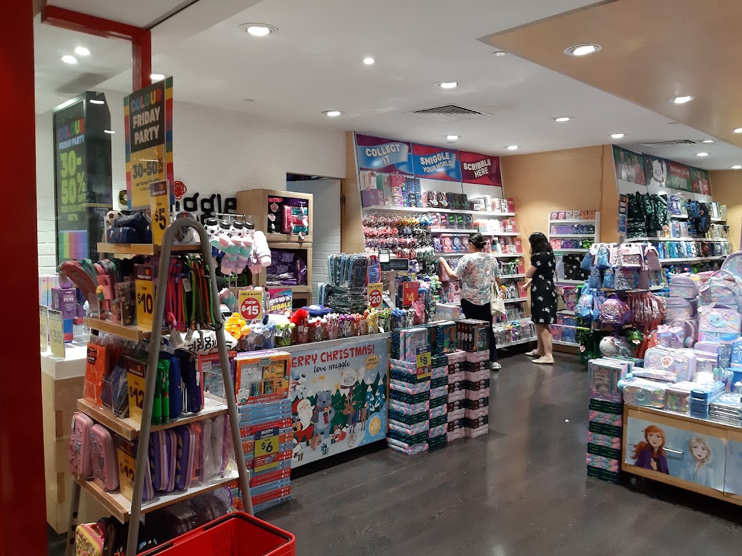 Interior view of Smiggle store showcasing colorful stationery, bags, and gifts, with customers browsing.