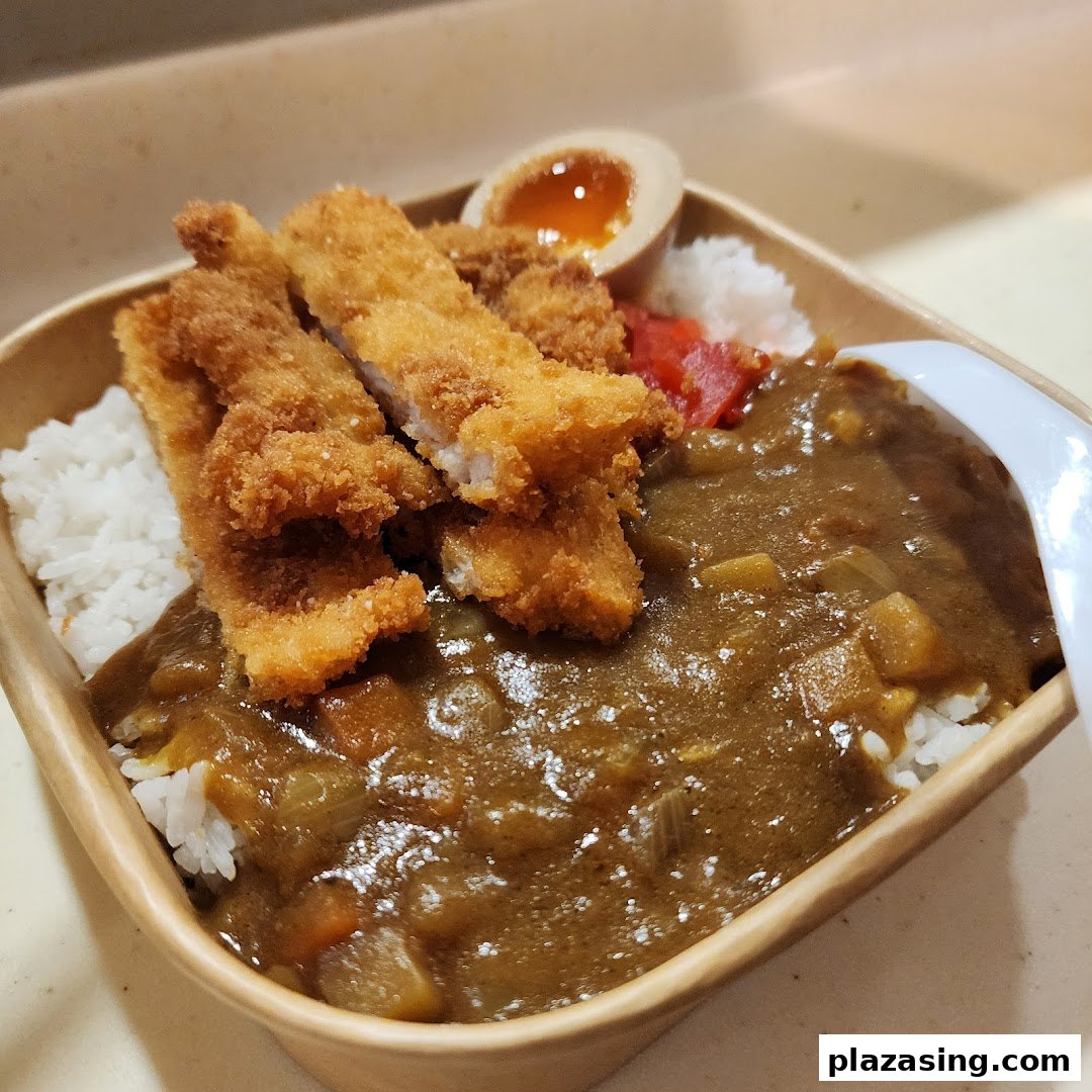 A delicious katsu curry rice bowl with crispy fried cutlets, a soft-boiled egg, and pickled ginger.