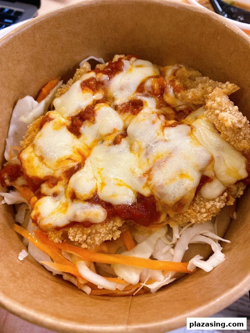 A close-up of a delicious snack bowl featuring crispy fried chicken, melted cheese, rich sauce, and fresh vegetables.
