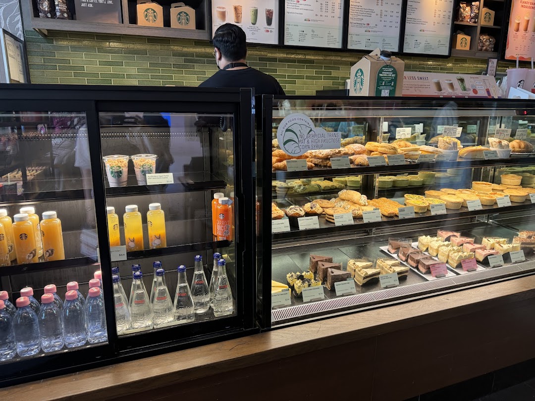 Interior view of Starbucks showcasing display cases filled with pastries, cakes, and bottled beverages.