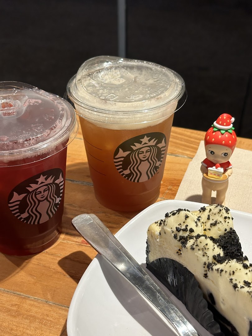 Two Starbucks beverages and a slice of cheesecake on a wooden table.