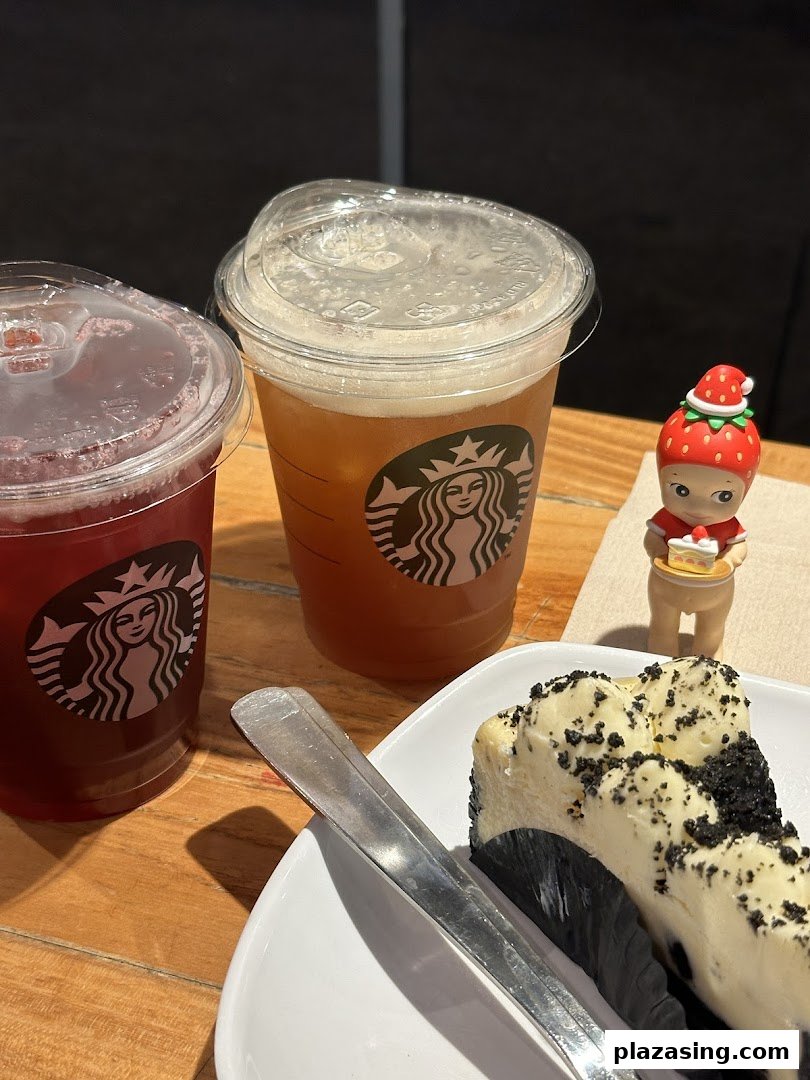Two Starbucks beverages and a slice of cheesecake on a wooden table.