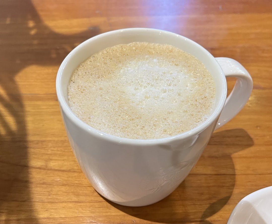 A close-up of a frothy beverage in a white mug on a wooden table.