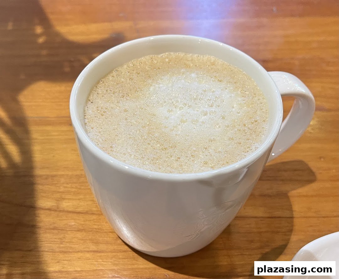 A close-up of a frothy beverage in a white mug on a wooden table.