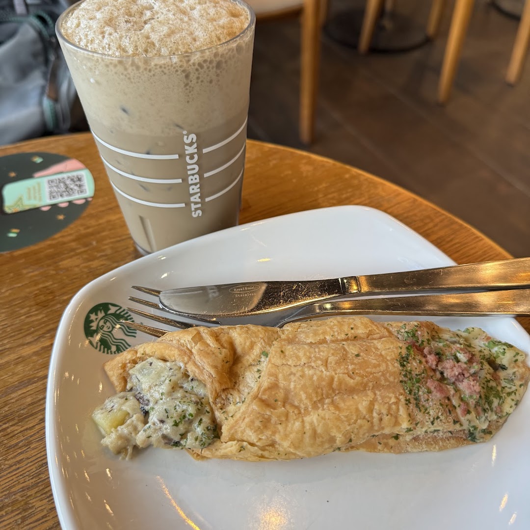 A Starbucks iced coffee and a savory pastry on a white plate with cutlery.