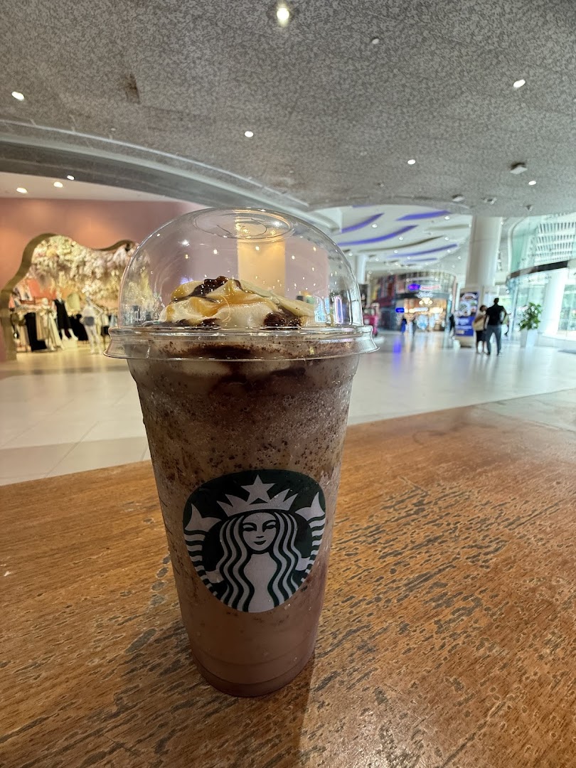 A Starbucks Frappuccino with whipped cream and caramel drizzle on a wooden table in a mall.