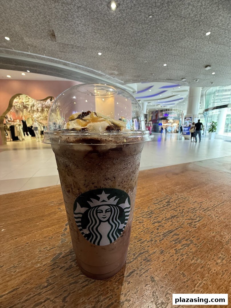 A Starbucks Frappuccino with whipped cream and caramel drizzle on a wooden table in a mall.