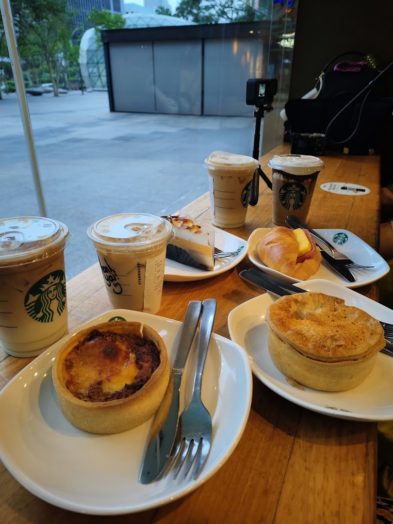 A table laden with Starbucks iced coffees, quiche, pie, and pastries, with an outdoor view.