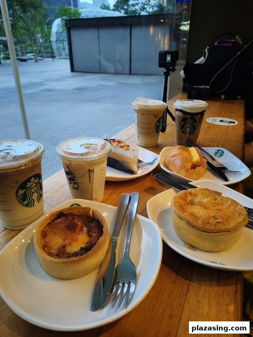 A table laden with Starbucks iced coffees, quiche, pie, and pastries, with an outdoor view.