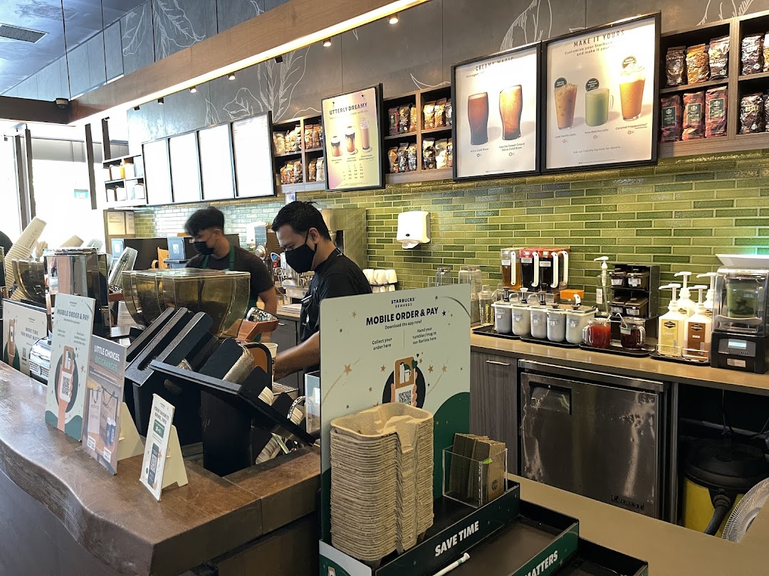 Interior view of Starbucks with baristas preparing drinks and promotional displays.