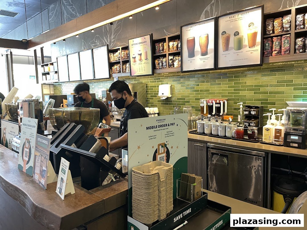 Interior view of Starbucks with baristas preparing drinks and promotional displays.