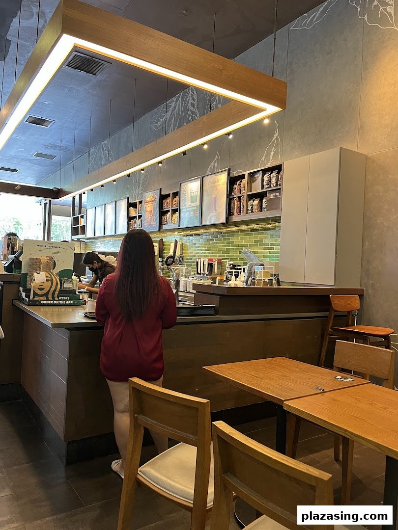 A customer orders at the counter inside Starbucks Plaza Singapura, with seating visible.