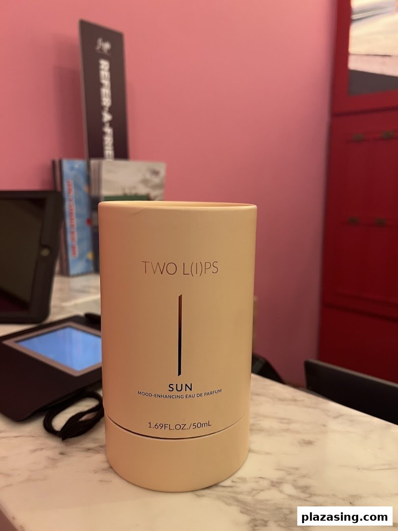 A product package for 'TWO L(I)PS SUN Mood-Enhancing Eau de Parfum' displayed on a counter.