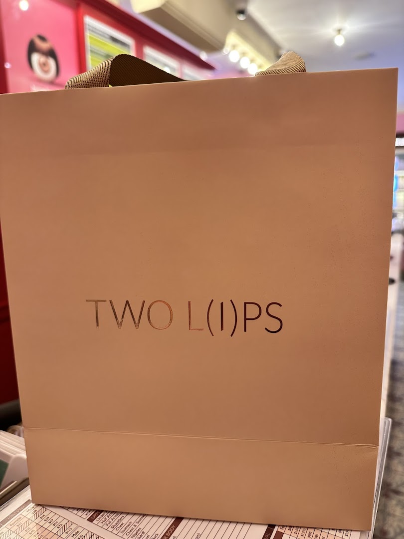 A light pink shopping bag with 'TWO L(I)PS' branding, likely from a beauty or body care shop.