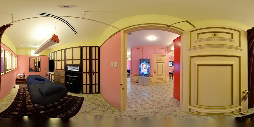 An interior view of a treatment room with a bed and a glimpse into a pink-walled hallway.