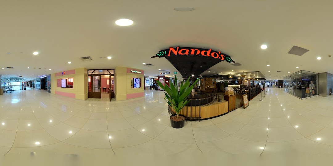 A brightly lit shopping mall corridor featuring various retail outlets and dining options like Nando's.