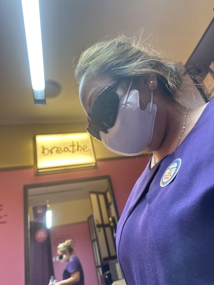 A person in a mask and purple uniform inside a treatment room with a 'breathe' sign.