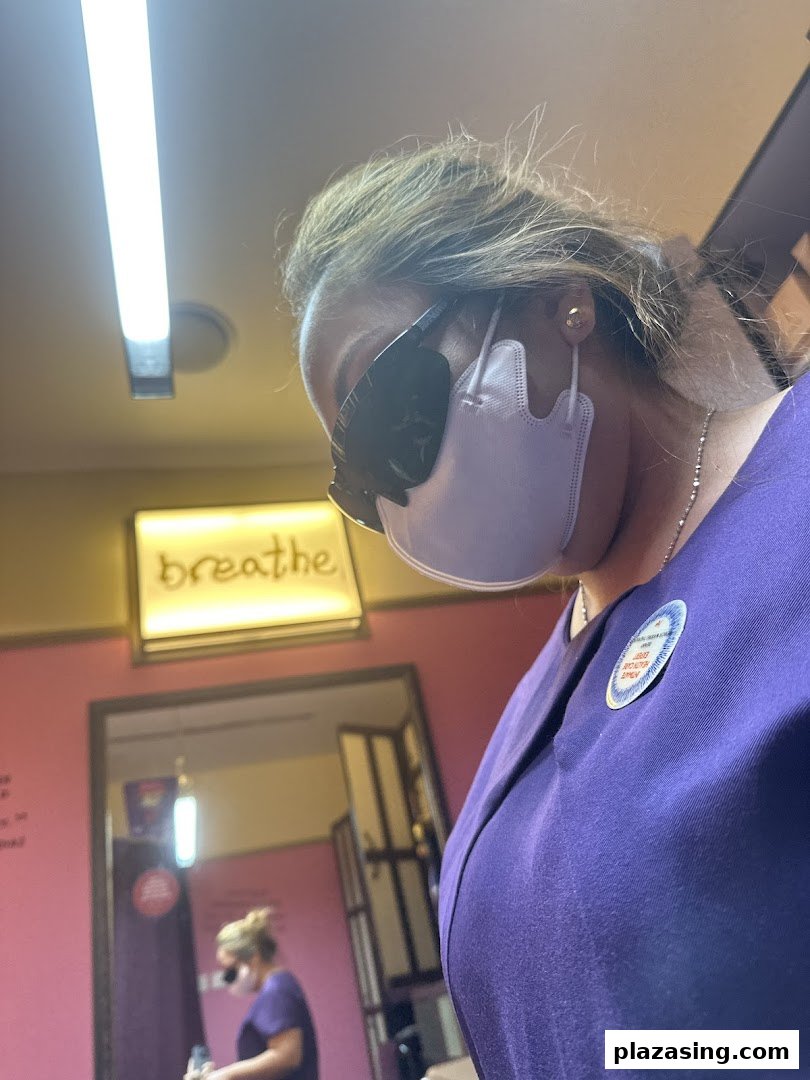 A person in a mask and purple uniform inside a treatment room with a 'breathe' sign.