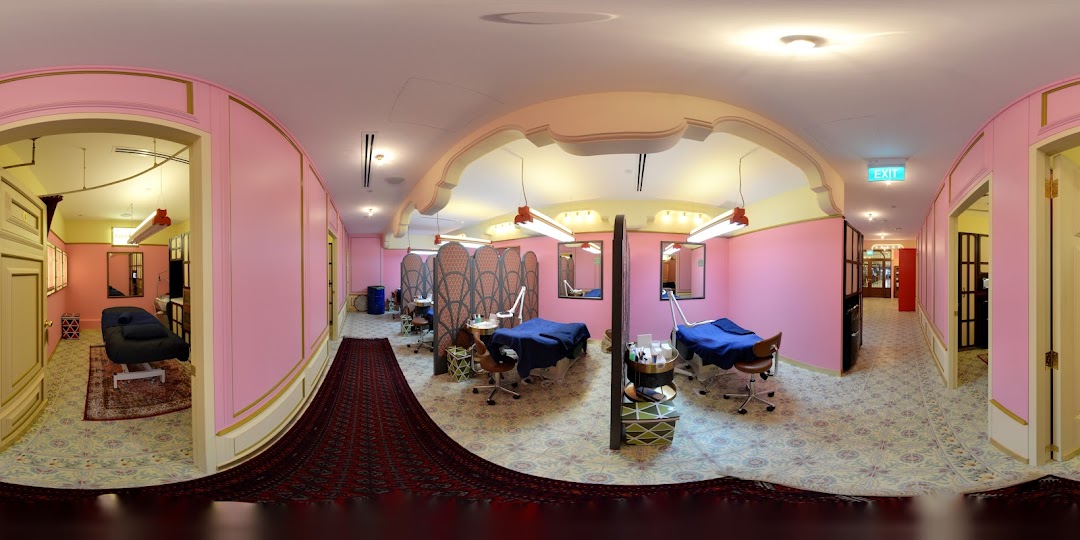 A panoramic view of Strip Co-Ed's vibrant pink interior with multiple private treatment rooms and beds.