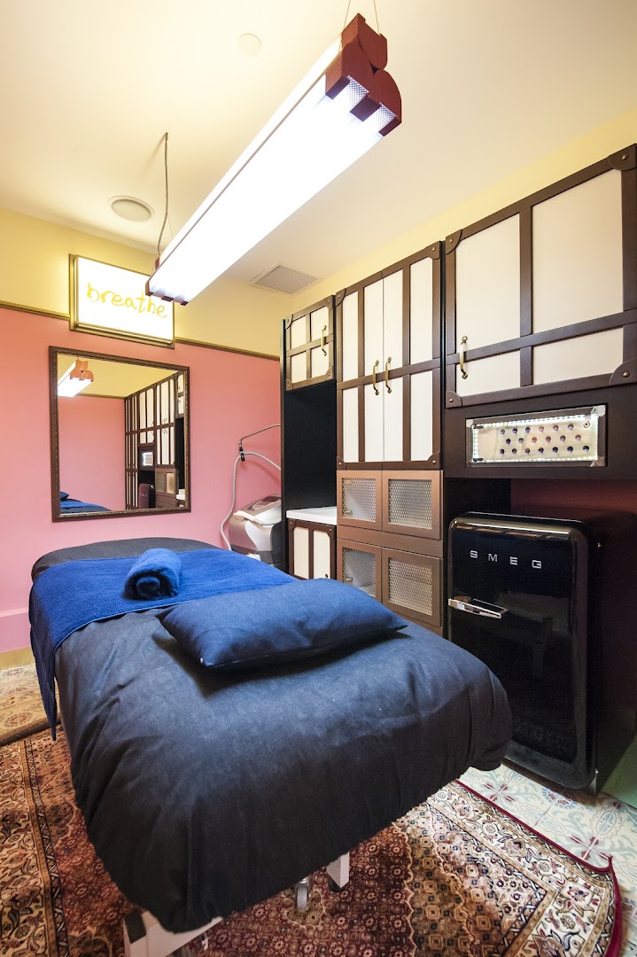 A cozy treatment room with a bed, 'breathe' sign, and stylish cabinets, suggesting a relaxing spa experience.