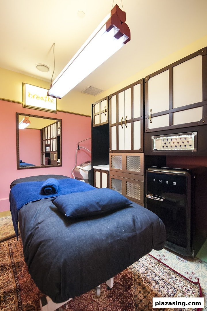 A cozy treatment room with a bed, 'breathe' sign, and stylish cabinets, suggesting a relaxing spa experience.