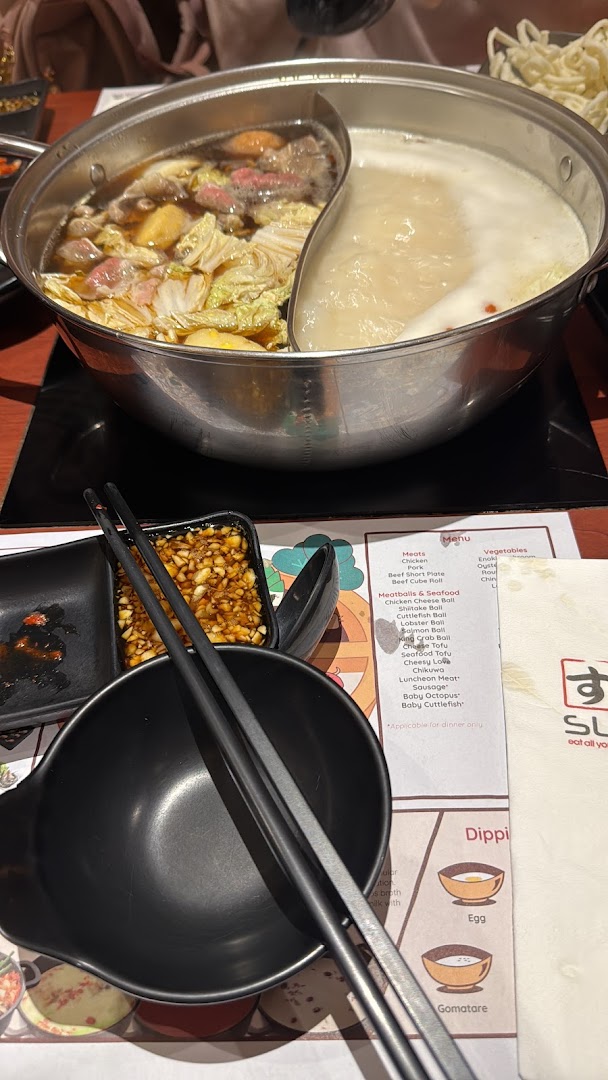 A bubbling hot pot with various ingredients and dipping sauces on a dining table at Suki-Ya.