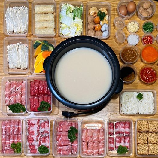 An overhead view of a shabu-shabu pot surrounded by fresh meats, vegetables, noodles, and various sauces.