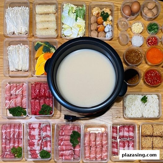 An overhead view of a shabu-shabu pot surrounded by fresh meats, vegetables, noodles, and various sauces.