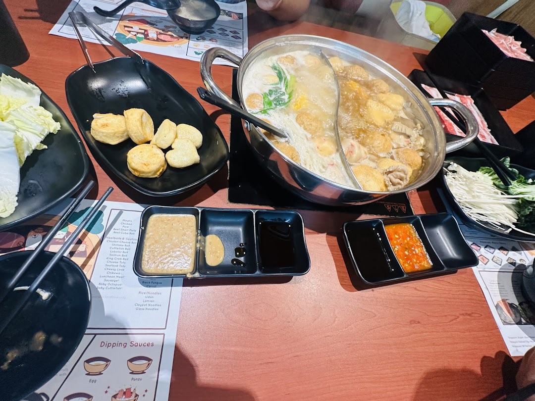 A vibrant hot pot meal with various ingredients, meats, and dipping sauces on a wooden table.