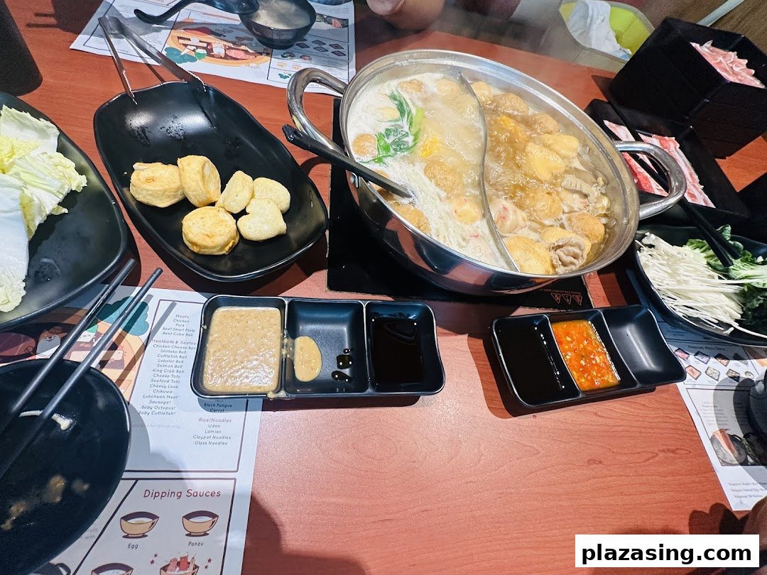 A vibrant hot pot meal with various ingredients, meats, and dipping sauces on a wooden table.
