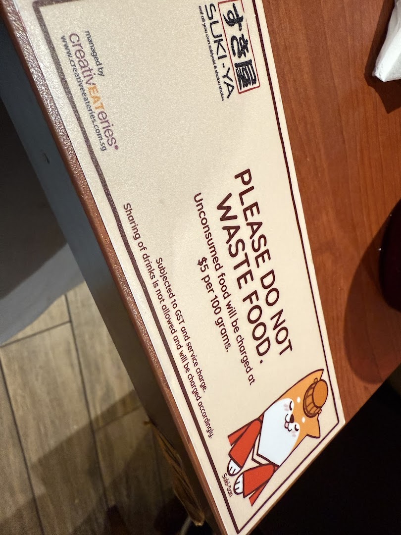 A sign from Suki-Ya detailing food waste policy and charges, featuring a cute Shiba Inu mascot.