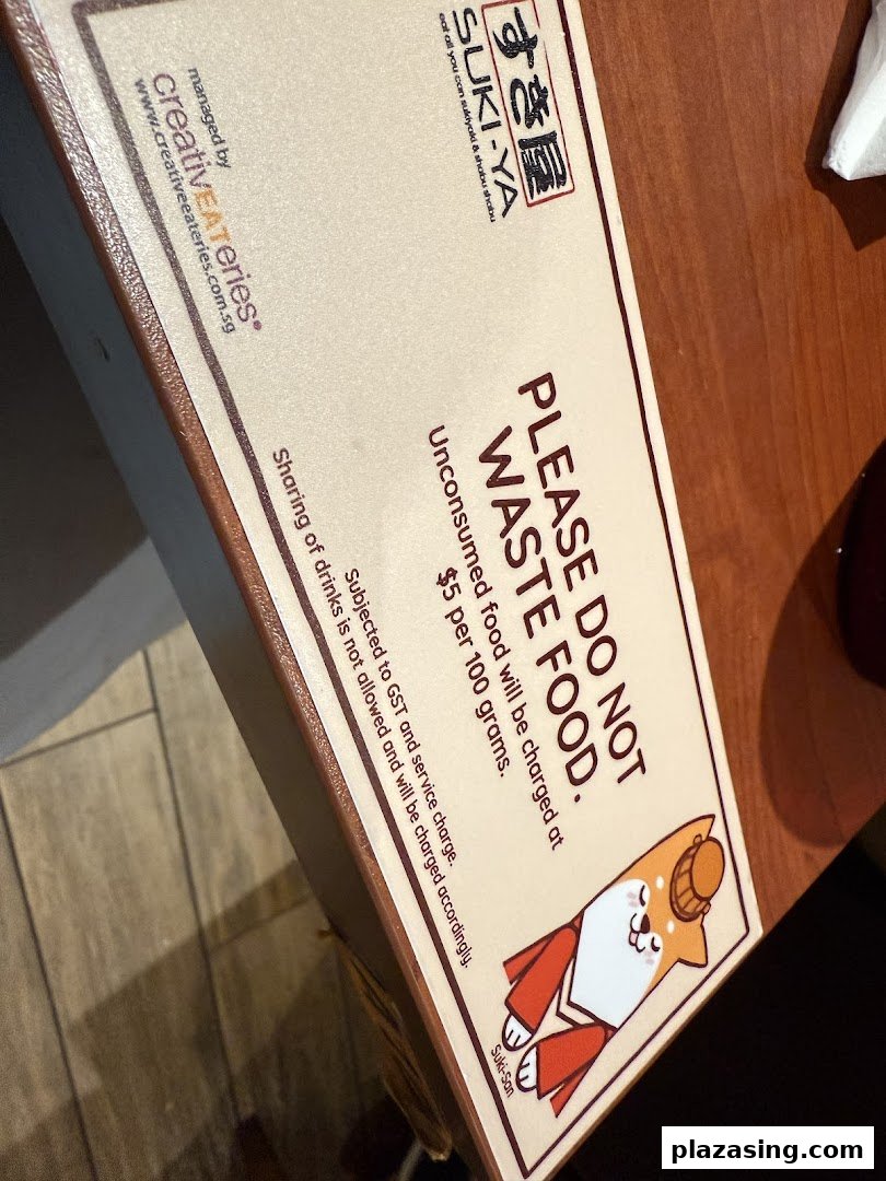 A sign from Suki-Ya detailing food waste policy and charges, featuring a cute Shiba Inu mascot.