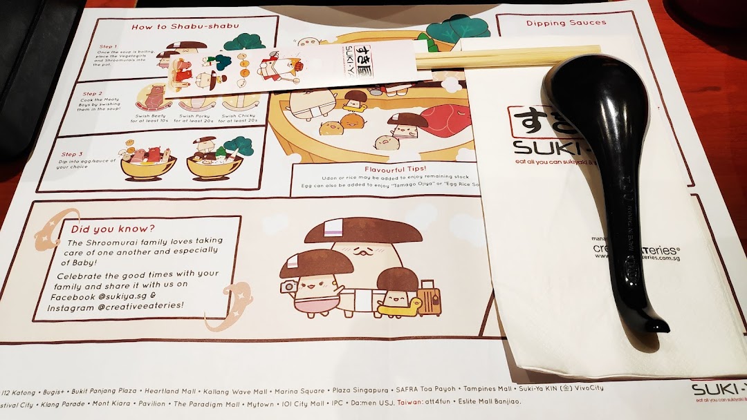 A Suki-Ya placemat detailing shabu-shabu cooking steps and tips, with chopsticks and a spoon.