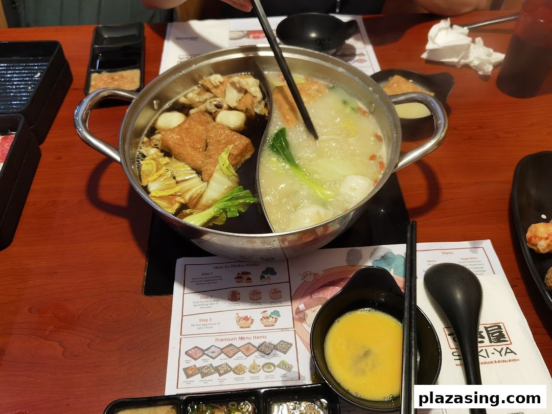 A close-up view of a bubbling hot pot with various ingredients on a dining table at Suki-Ya.